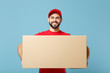 © ViDi Studio - Delivery man in red uniform isolated on blue background, studio portrait. Male employee in cap t-shirt print working as courier dealer hold empty cardboard box. Service concept. Mock up copy space.