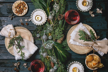 Wall Mural - Christmas or New year table setting with empty ceramic plates, wine glasses, napkins, Christmas thuja wreath, luminous garland and burning candles on dark wooden plank table. Holiday mood flat lay