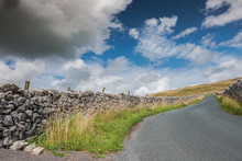 Low Level View Of A Rural Asphalt Road, Appearing Deserted Ascending A Mountain In The Yorkshire Dales. Dry Stoned Wall Can Be Seen Extending To The Distance.