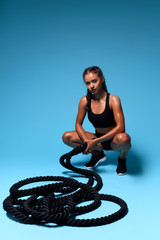 Wall Mural - Portrait of a sexy young woman in fashion black sportswear looking exhausted and defeated while sitting at cross-training gym. full length photo. isolated blue background, studio shot. free tima