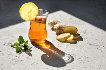 useful tonic tea . Traditional drink tea in a glass glass with mint lemon and ginger on a light background with contrasting hard shadows .