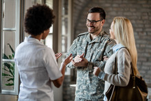Happy Military Man And His Wife Talking To A Doctor At Medical Clinic.