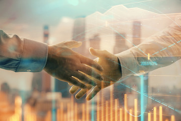 Double exposure of financial graph on cityscape background with two businessman handshake. Concept of stock market deal