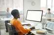 © Seventyfour - Side view portrait of young African-American man using computer in office, focus on blank white screen, copy space