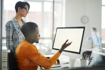 Wall Mural - Side view portrait of young African-American man looking at blank computer screen while discussing IT project with female colleague, copy space