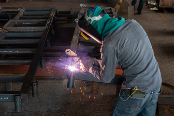 The welder is welding a steel structure with the process Flux Cored Arc Welding (FCAW) in Industrial factory.