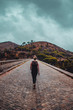 Back view of a travel girl walking on a cobble stone road of a lake dam on a moody dark vacation day with rain and dramatic clouds. Serra de Monchique, Algarve in Portugal
