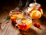 Fruit hot tea with the addition of oranges, lemons, mandarins and raspberries in a glass cups on a  wooden table. Healthy hot drink