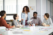 © Seventyfour - Diverse group of business people sharing ideas while sitting at table in modern office, focus on curly-haired young woman gesturing actively