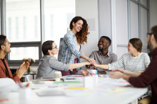 Portrait Of Creative Business Team Stacking Hands Over Meeting Table, Focus On Smiling Young Woman Standing In Center