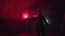 Man Lighting His Way Inside Dark Cave With A Burning Signal Flare And Leaving The Entrance Behind Him. Stock Footage. Dangerous Tourism Inside Dark Grotto.