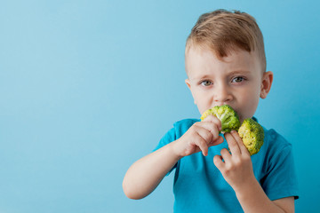 Wall Mural - Little kid holding broccoli in his hands on blue background. Vegan and healthy concept