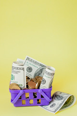 Wall Mural - Shopping basket with coins and dollar bills on yellow background. Space for text. Close up. Business concept.