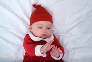 Baby in santa hat lying on a white background, plays with his hands. Christmas concept.