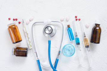 Wall Mural - Syringe, stethoscope, thermometer, various tablets and bottle with blue liquid on a white background. Medical flat lay background.