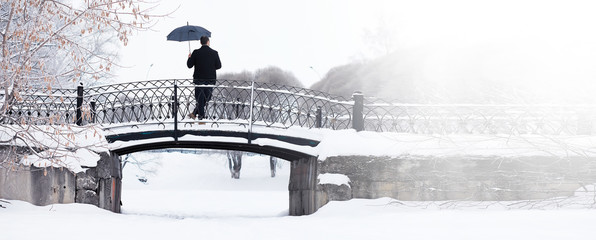 Wall Mural - Winter walk with an umbrella.Man in a coat with an umbrella, walk against the backdrop of the winter landscape, winter view