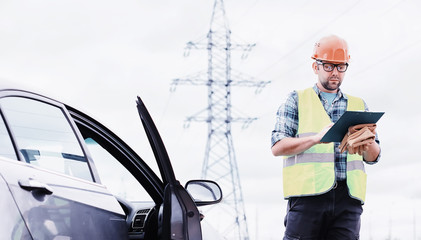 A man in a helmet and uniform, an electrician in the field. Professional electrician engineer inspects power lines during work.