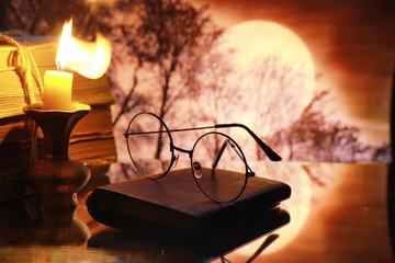 Wall Mural - Vintage glasses on an old retro book on a background of the moon. Reading a book by candlelight. The concept of book thrillers and novels.