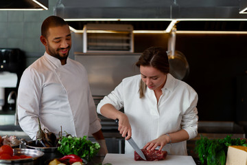 Wall Mural - Handsome young African chef is cooking together with his Caucasian girlfriend in the kitchen using red wine as an ingredient.