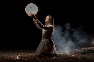 beautiful young girl on a night beach with sand and stars holds the moon in her hands