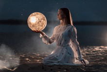 Beautiful Young Girl On A Night Beach With Sand And Stars Holds The Moon In Her Hands