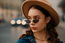 Outdoor Close Up Fashion Portrait Of Young Elegant Lady Wearing Beige Hat, Trendy Sunglasses, Earrings, Chain Necklace, Denim Shirt, Posing In Street Of European City. Copy, Empty Space For Text