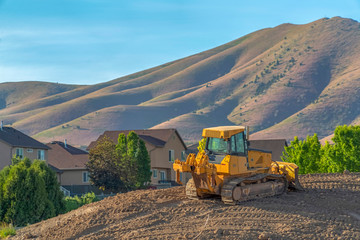 Wall Mural - Yellow bulldozer on a construction site overlooking homes mountain and sky