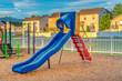 Blue slide with red stairs at a playground against homes mountain and blue sky