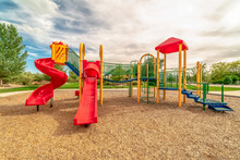 Focus On Empty Childrens Playground At A Park With Red Slides And Climbing Bars