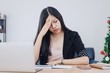 © bunditinay - Beautiful young Asian girl feeling headache and stress in office space with laptop and decorate christmas tree background.Concept of Healthcare and Office syndrome.