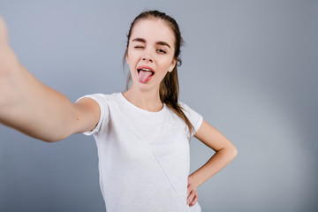 beautiful brunette girl wearing white shirt making selfie isolated over grey