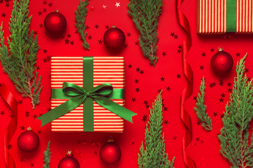 Wall Mural - Christmas background. Gift with green ribbon red balls christmas tree branches confetti stars on red background top view. New Year presents Festive decorations Flat lay Xmas holiday 2020 celebration