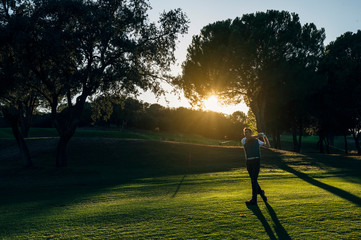 Male golf player teeing off golf ball from tee box to beautiful sunset