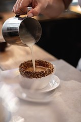 Sticker - High angle shot of a barista making coffee with milk in a white cup partially covered in chocolate