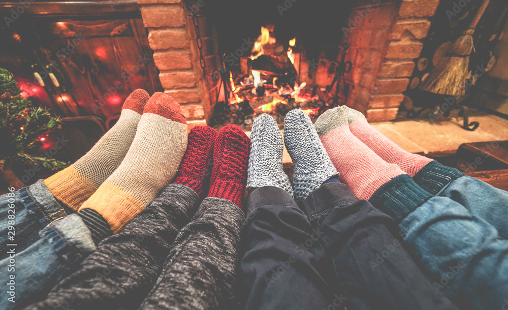 Legs view of happy family lying down next fire place wearing warm wool socks - Winter, holiday, love and cozy concept - Focus on feet - obrazy, fototapety, plakaty 
