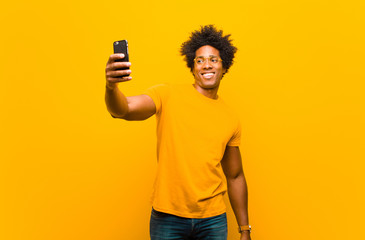 Wall Mural - young african american man with a smart phone against orange bac