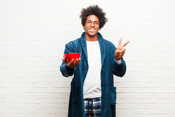 Wall Mural - young black man wearing pajamas with a breakfast bowl against br