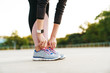 © Drobot Dean - Cropped image of woman wearing tracksuit touching her sneakers outdoors