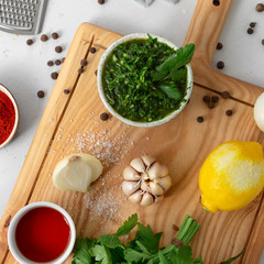 Wall Mural - Cooking background. Raw ingredients for preparation Argentinian green Chimichurri or Chimmichurri salsa or sauce on white wooden table