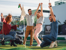 Group Of Smiling Friends Enjoying Together Playing Mini Golf In The City.
