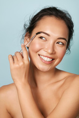 Wall Mural - makeup. woman brushing brows with eyebrow brush closeup. portrait of happy smiling asian girl model 