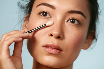 beauty. woman applying makeup on skin with cosmetic brush closeup. portrait of asian female model wi