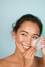 Face Skin Care. Smiling Woman Using Facial Oil Blotting Paper Portrait. Closeup Of Beautiful Happy Asian Girl Model With Natural Makeup Using Oil Absorbing Sheets, Beauty Product At Studio