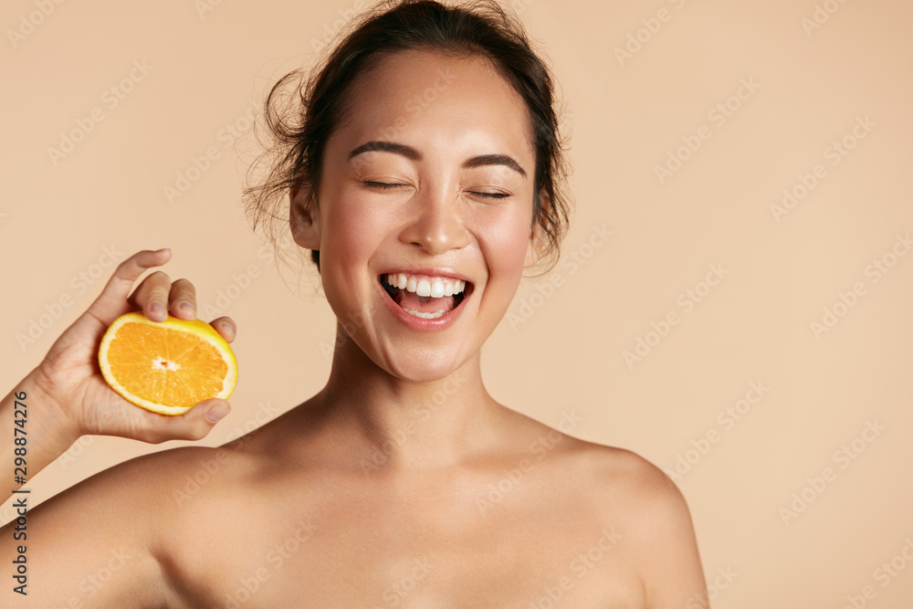 Beauty. Smiling woman with radiant face skin and orange portrait. Beautiful smiling asian girl model with natural makeup, healthy smile and glowing hydrated facial skin. Vitamin C cosmetics concept - obrazy, fototapety, plakaty 