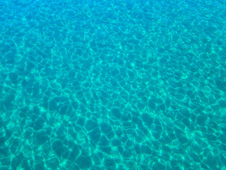  Aerial view of a sandy seabed, crystal clear blue water, reflections of the sun cause ripples on the sea surface. Texture and background. Pool
