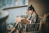 Fototapeta Natura - Woman sitting on hotel's balcony and using her smartphone 