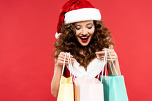 Excited Curly Girl In Santa Costume Posing With Shopping Bags, Isolated On Red