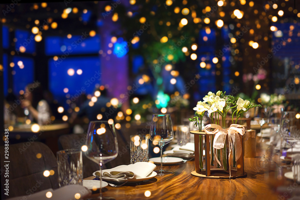 Blurred party background with served table with bouquet of flowers and people sitting at restaurant, bar or night club with colorful lights bokeh. - obrazy, fototapety, plakaty 