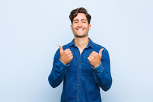 Young Handsome Man Smiling Joyfully And Looking Happy, Feeling Carefree And Positive With Both Thumbs Up Against Blue Background
