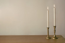 Two Candles Burning In Vintage Candlesticks On Table Against Empty Wall. .